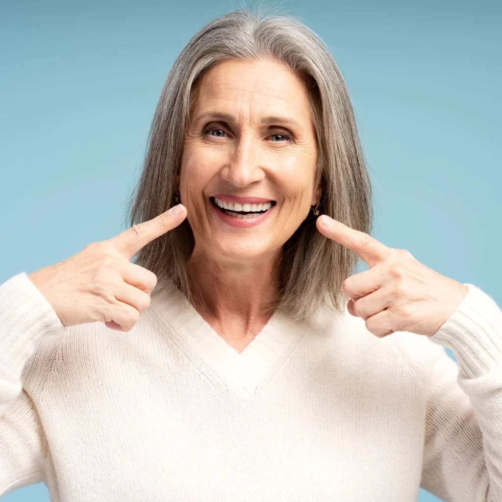 Senior woman smiling and pointing to teeth after professional teeth whitening in Punta Gorda, FL